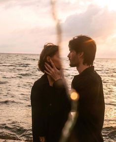 a man and woman standing next to each other near the ocean with their hands on their face