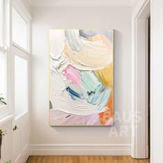 an abstract painting hangs on the wall in a white room with wooden floors and large windows