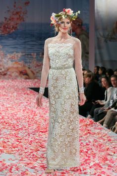 a woman is walking down the runway wearing a dress with flowers in her hair and headpiece