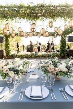 a table set for an outdoor wedding with white flowers and greenery on the tables