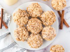 a white plate topped with cookies next to cinnamon sticks and an orange juice in the background