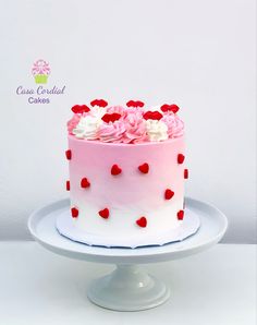 a pink and white cake with red hearts on the top is sitting on a plate