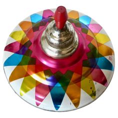 a multicolored metal object with a red button on it's center piece