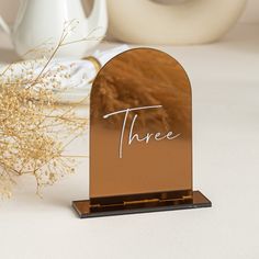 there is a small wooden stand with the word three written on it next to some dried flowers