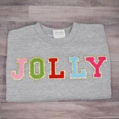 a grey shirt with the word jolly written in multicolored letters