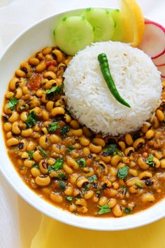 a white bowl filled with beans and rice on top of a yellow table cloth next to sliced cucumbers