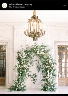 a chandelier hanging from the ceiling in front of a white room with flowers and greenery