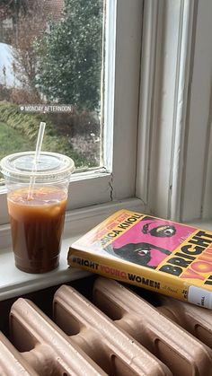 a book and drink sitting on a window sill next to a radiator