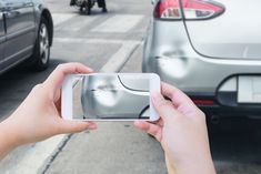 a person holding up a smart phone to take a photo of cars on the street