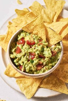 a bowl filled with guacamole surrounded by tortilla chips on a plate