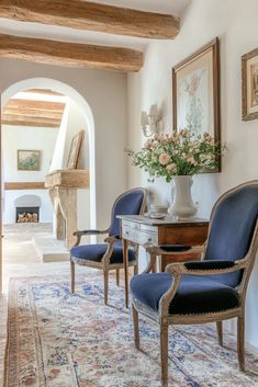 two blue chairs sitting on top of a rug in front of a table with flowers