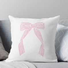 a pink bow on a white pillow sitting on top of a gray couch next to pillows