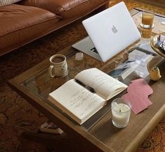 a coffee table with an open book, candle and laptop on it in front of a leather couch