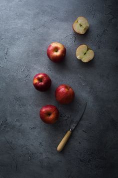 some apples and a knife are on a gray table with a black surface, top view