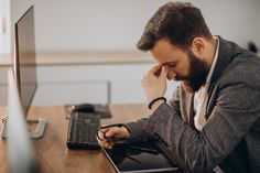 a man sitting in front of a laptop computer with his hand on his face while looking at the screen