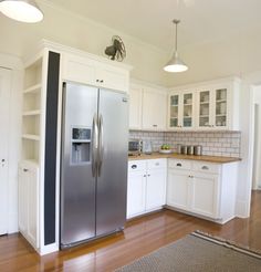 a kitchen with white cabinets and stainless steel refrigerator freezer combo in the center, along with hardwood flooring