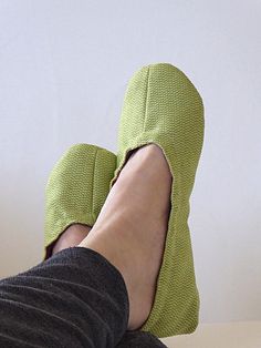 a person's feet wearing green slippers and black pants sitting on a table