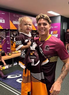 a man holding a small child in his arms while standing next to another person wearing purple and orange jerseys