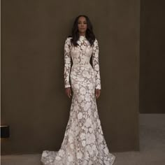 a woman standing in front of a wall wearing a white dress with flowers on it