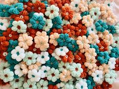 many crocheted flowers are arranged together on a tablecloth with white, orange and green colors