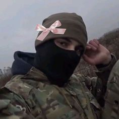 a man in camouflage with a pink bow on his head wearing a black face mask