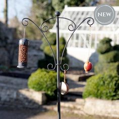 a bird feeder with an apple hanging from it's side next to a garden