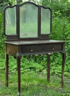 an old vanity with a mirror on it in the grass near some bushes and trees