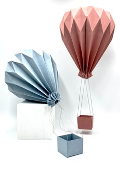 two origami hot air balloons and a box on a white background, one with a string attached to it