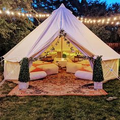 a white tent is set up in the middle of a yard with lights strung over it