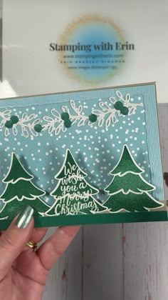 someone is holding up a christmas card with trees and snowflakes on it in front of a white background