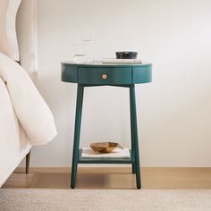 a small blue table with a bowl on it next to a white bed and nightstand