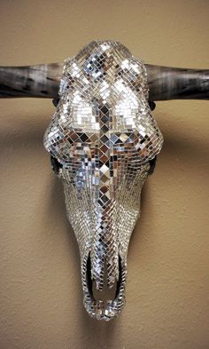 a cow skull mounted to the side of a wall next to a wooden stick with sequins on it