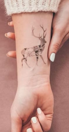 a woman's hand with a deer tattoo on her left wrist and the other hand holding