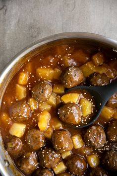 meatballs and pineapple stew in a pot with a spoon