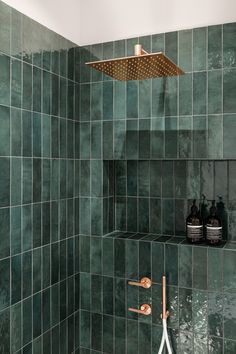 a green tiled shower with copper faucet and soap dispenser in the corner