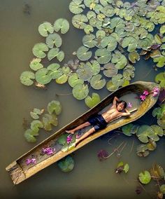 a man is floating in a boat on the water with lily pads and leaves around him