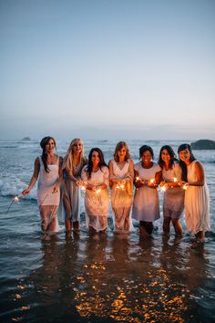 a group of women standing in the ocean holding sparklers