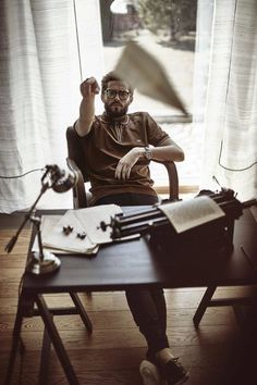 a man sitting at a desk in front of a window with an old typewriter