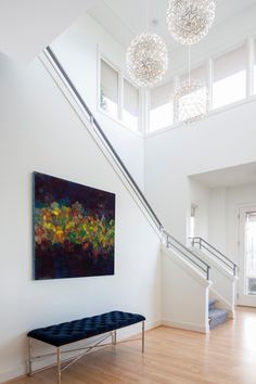 a painting on the wall next to a bench in a room with stairs and chandeliers