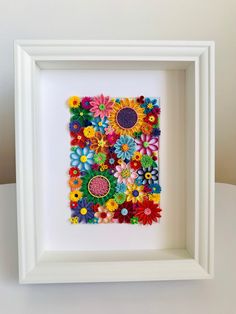 a white frame filled with colorful flowers on top of a table next to a wall