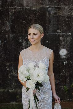 a woman in a wedding dress holding a bouquet of white flowers and smiling at the camera