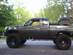 a gray truck parked on the side of a road with large tires in it's bed