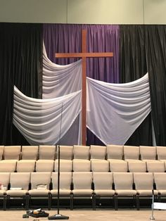 an empty church with white chairs and a cross on the back wall, in front of black drapes