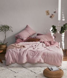 a bed with pink sheets and pillows in a room next to a plant on the floor