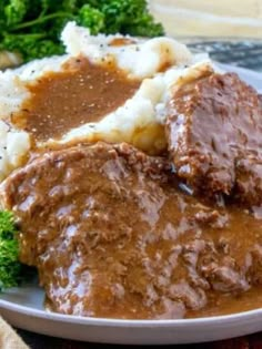 a white plate topped with meat and gravy covered in gravy next to broccoli