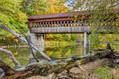 a covered bridge over a river surrounded by trees and fallen down branches in the fall