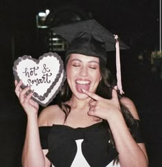 a woman in graduation cap and gown holding a heart shaped cake with writing on it