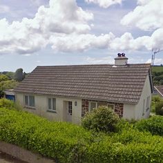 a small house with a tiled roof surrounded by greenery and shrubs on a sunny day