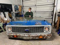 a man standing in front of an old blue truck with rust on it's hood