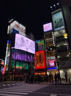 people are standing in the middle of an intersection at night with brightly lit buildings behind them